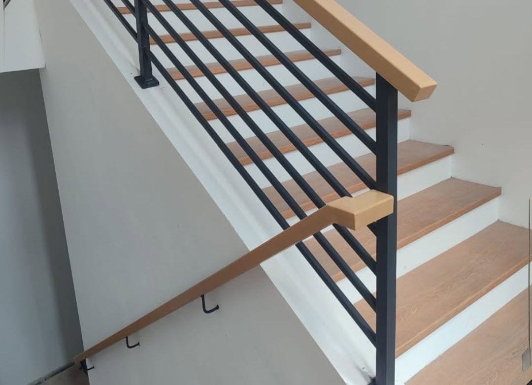 A flat black steel bar railing with a timber handrail beside a flight of timber treads.