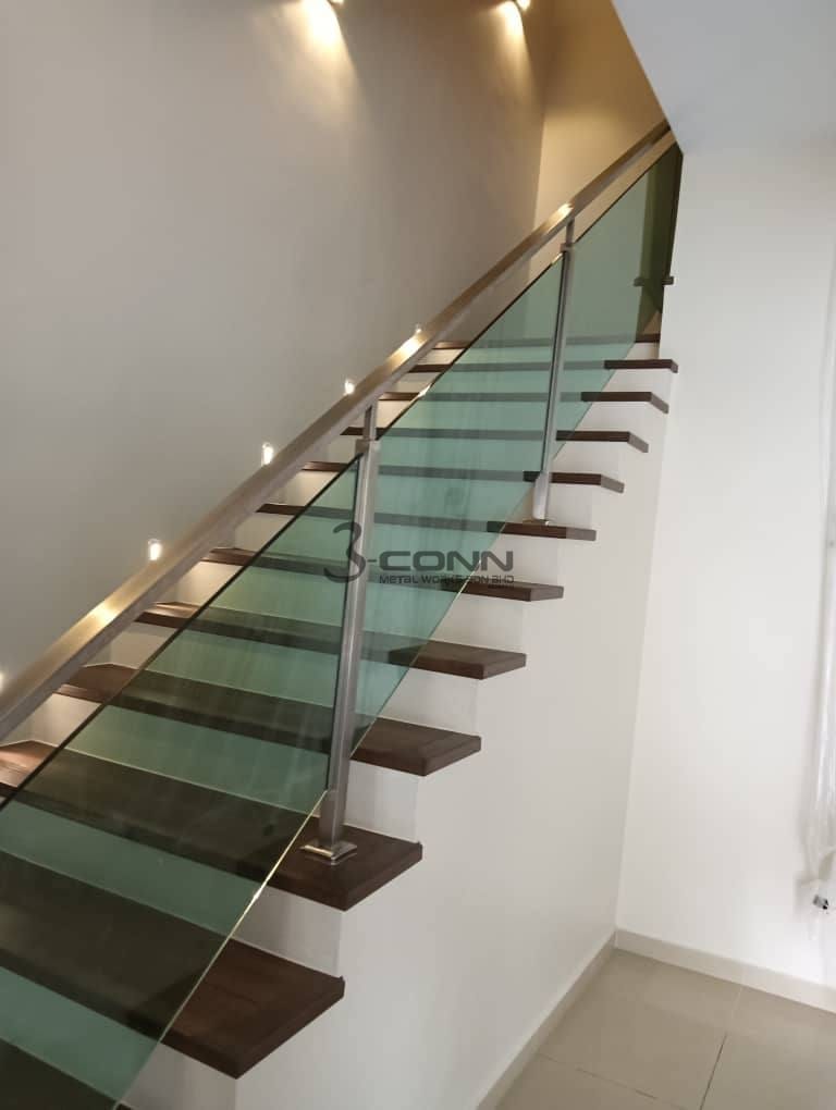 A staircase with a clear tempered glass railing in a slim steel frame, lit from below.
