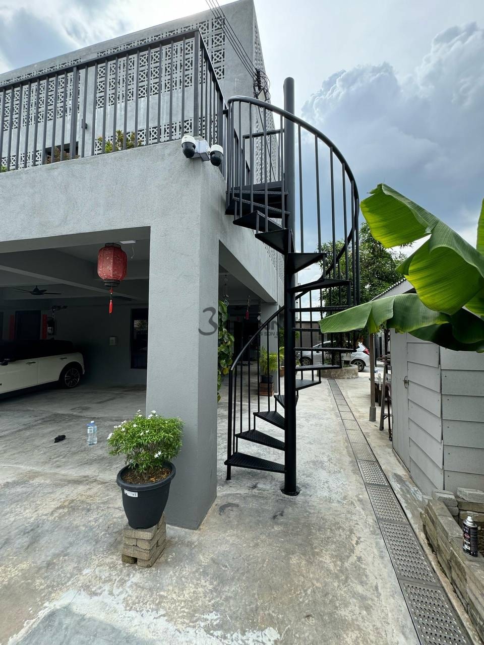 A black mild steel spiral staircase with chequer-plate treads rising outside a house beside a banana plant.