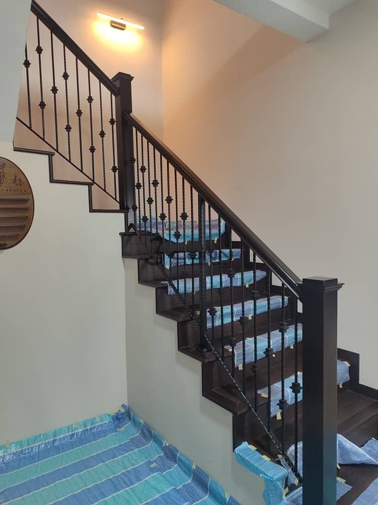 A wrought iron railing with scrolled balusters and a dark timber handrail on a curved flight.
