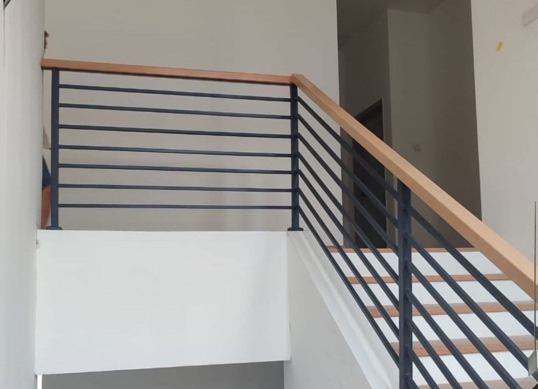 A flat black steel horizontal-bar railing with a timber handrail at a landing.