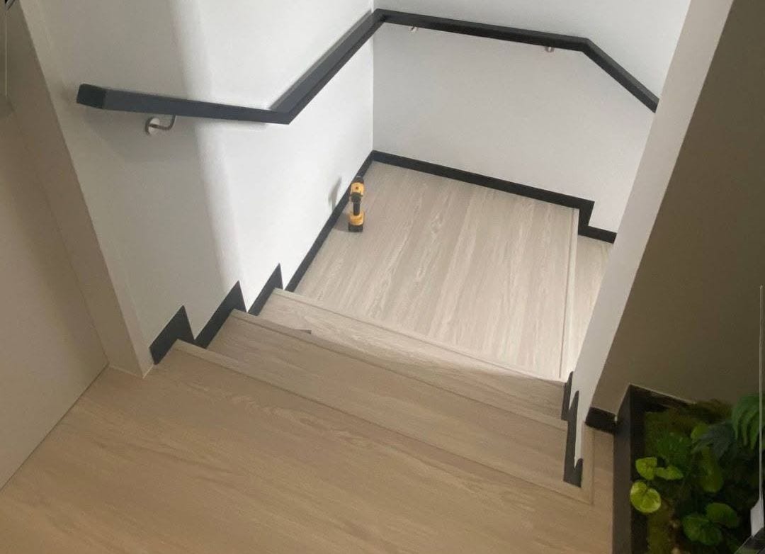 A slim black steel wall handrail turning the corner of a landing above pale timber treads.